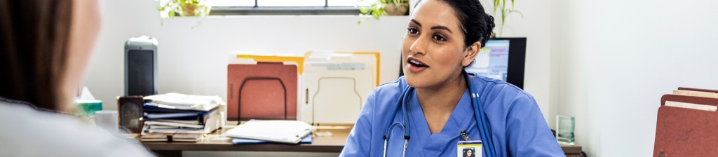 Health Informatics professional sitting at desk speaking with person across from her