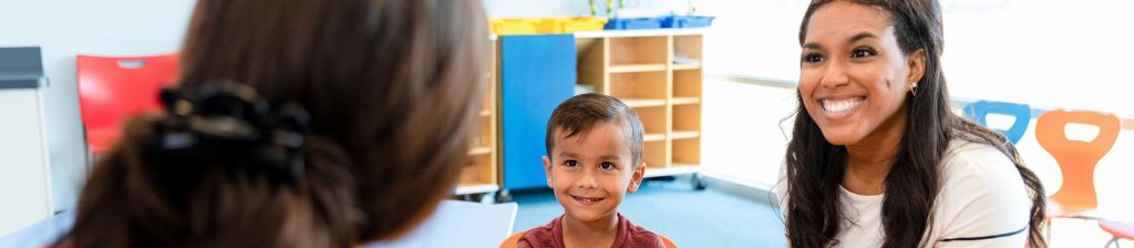 Hispanic mother and preschool aged son smiling at teacher in classroom